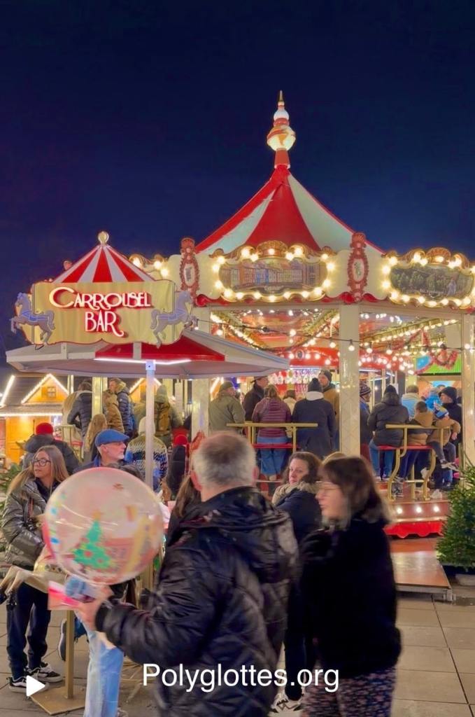 Un carrousel illuminé avec des gens se rassemblant autour, dans une atmosphère festive de marché de Noël.
